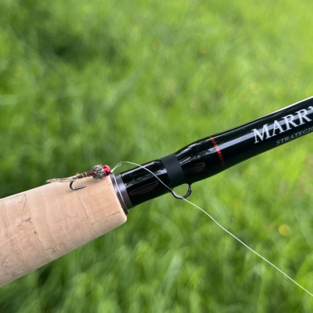 Petite nymphe de pêche à la mouche rouge posées sur une canne à pêche de la marque Marryat de Thibaut Le Sceller de Pesketa